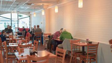 A restaurant with wooden tables and chairs, white brick walls, and pendant lighting.