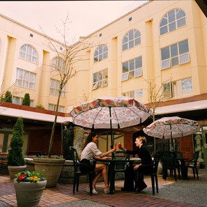 Ein Terrassenbereich im Freien mit Tischen, Stühlen, Sonnenschirmen und Topfpflanzen.