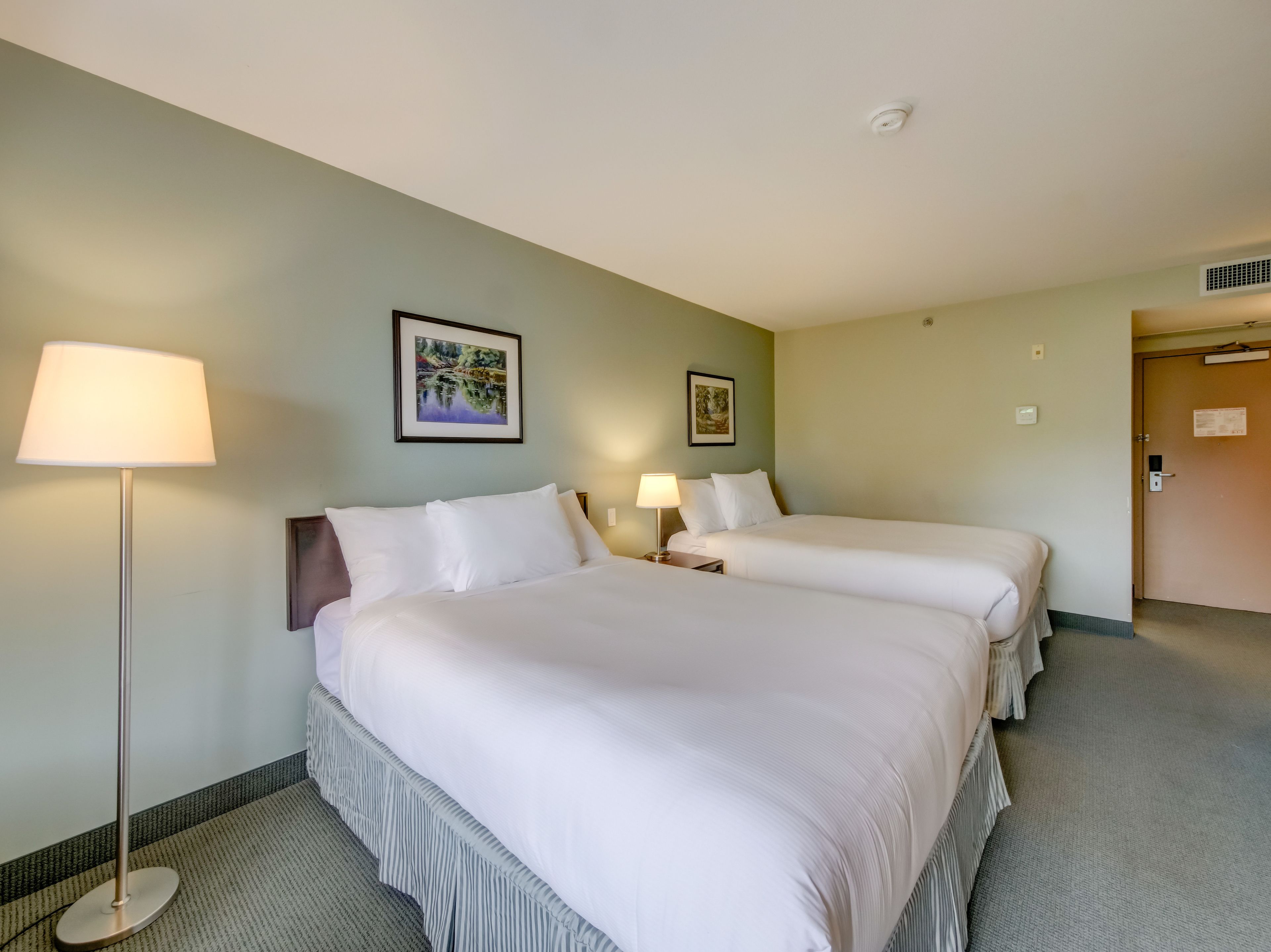 Een hotelkamer met twee bedden, een staande lamp en twee wandlampen.