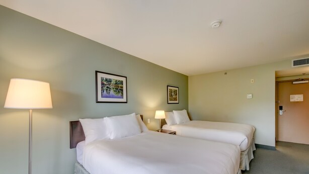 Ein Hotelzimmer mit zwei Betten, einer Stehlampe und zwei Wandleuchten.