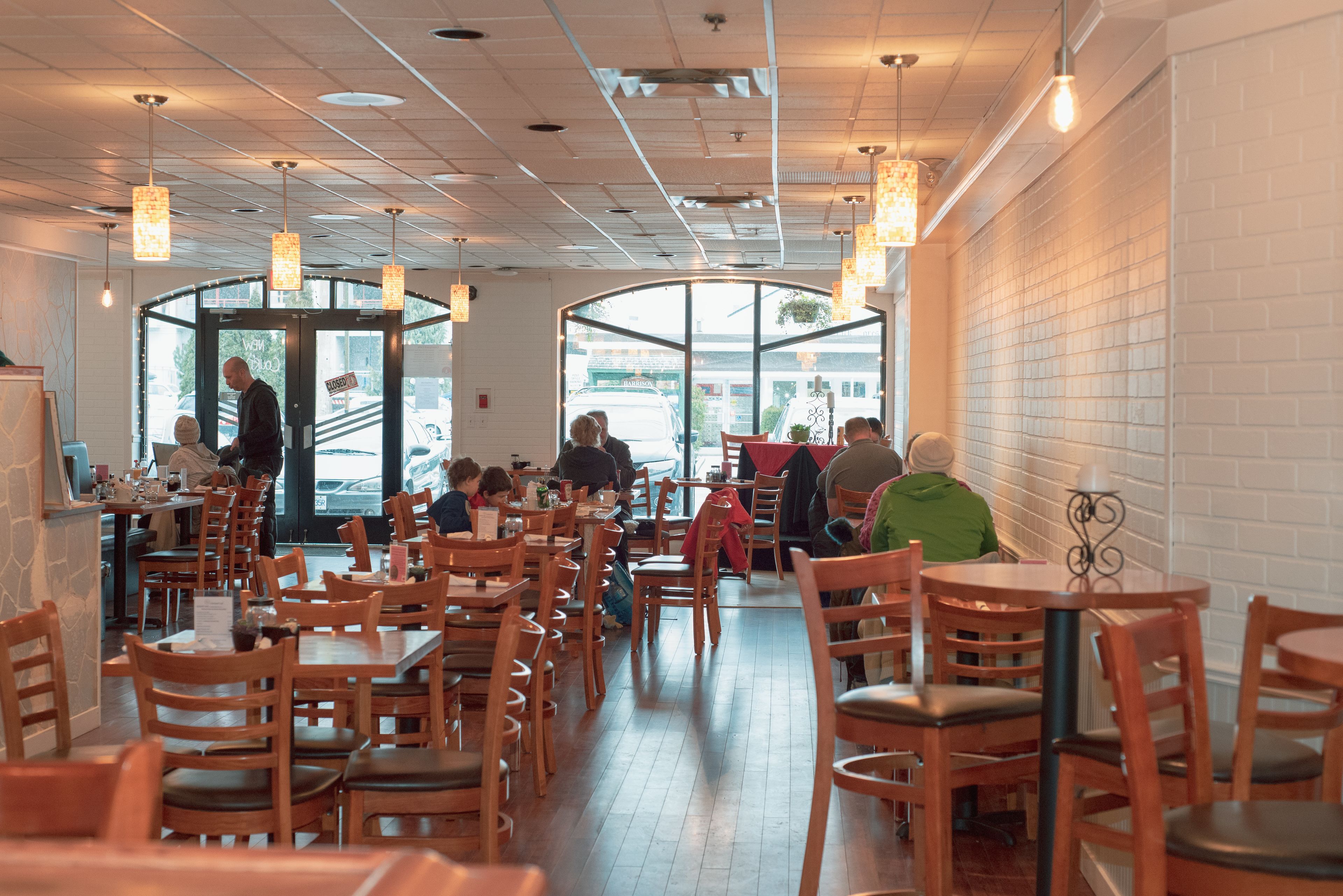 A restaurant with wooden tables and chairs, large windows, and hanging pendant lights.