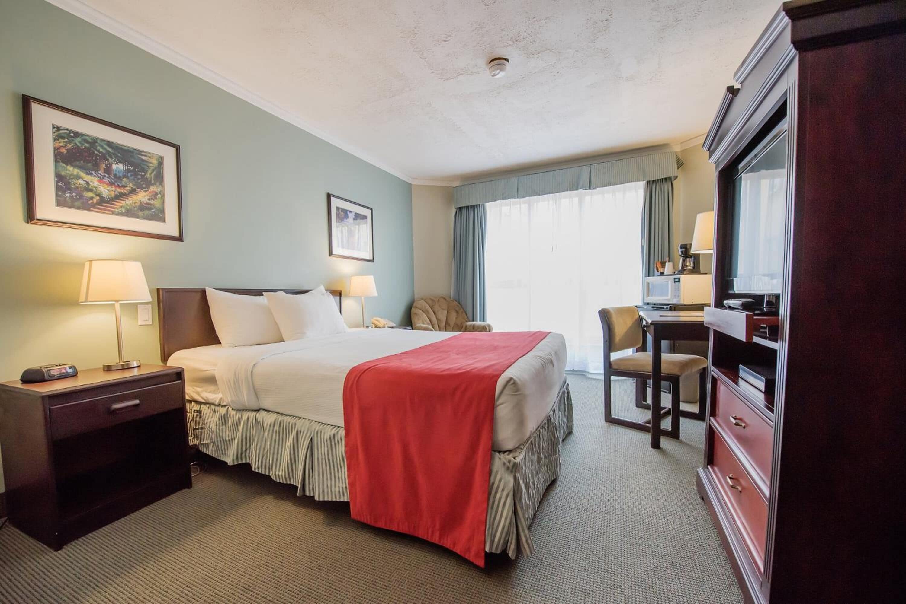 A hotel room with a bed, bedside tables, a desk, a chair, a dresser, and a large mirror.