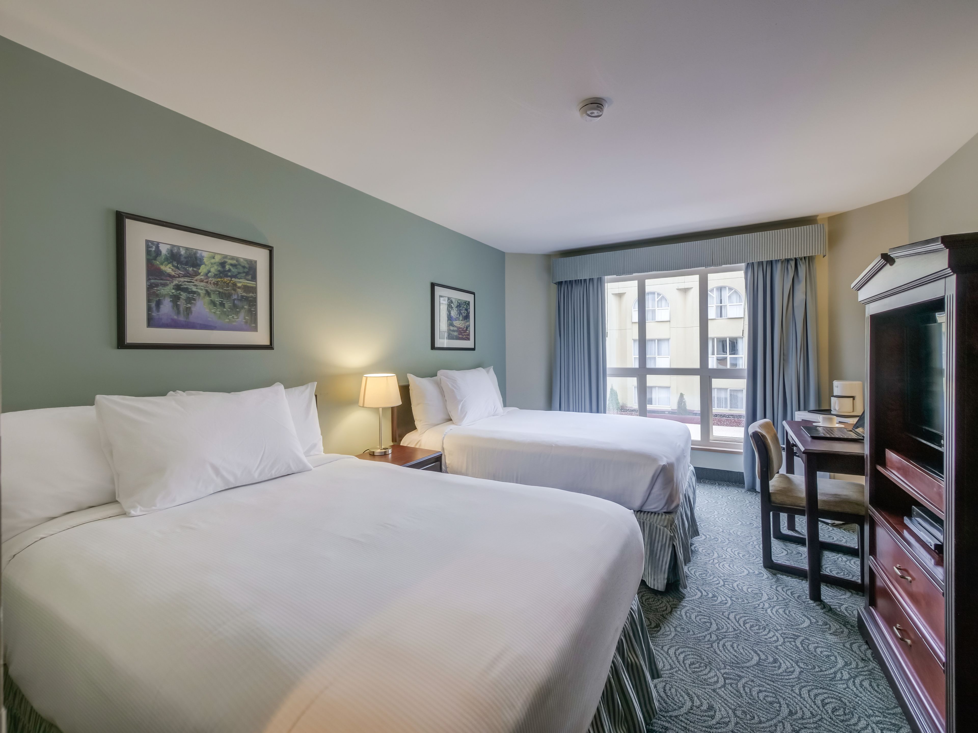 Habitación de hotel con dos camas, un escritorio con silla, televisión y ventana con cortinas.
