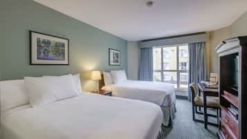 Habitación de hotel con dos camas, un escritorio con silla, televisión y ventana con cortinas.