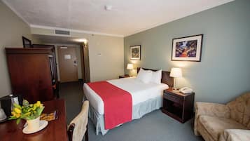 A hotel room with a bed, bedside tables, a desk with a chair, a couch, and a dining table with a vase of flowers.