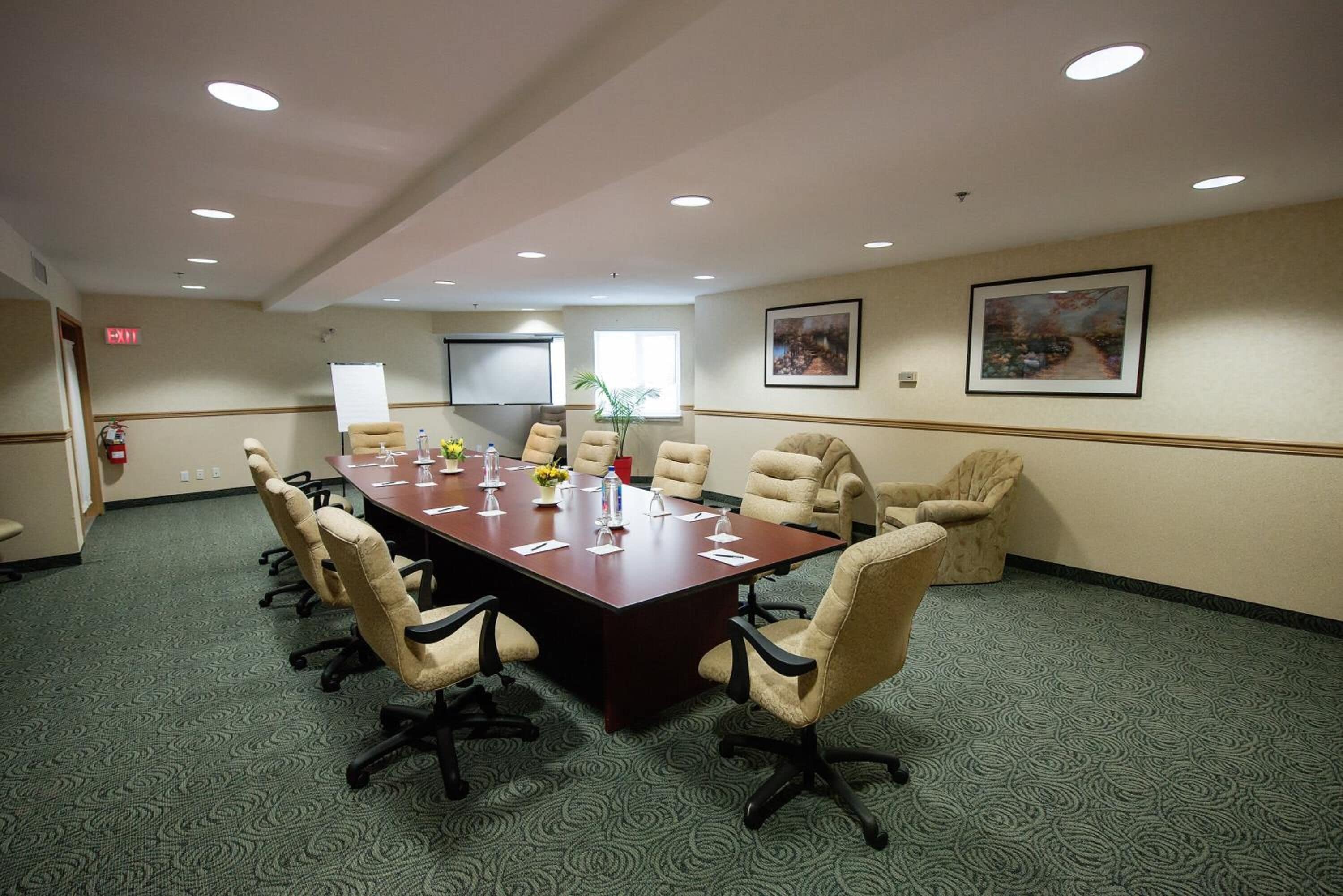 A conference room with a long table, beige chairs, and a projector screen.