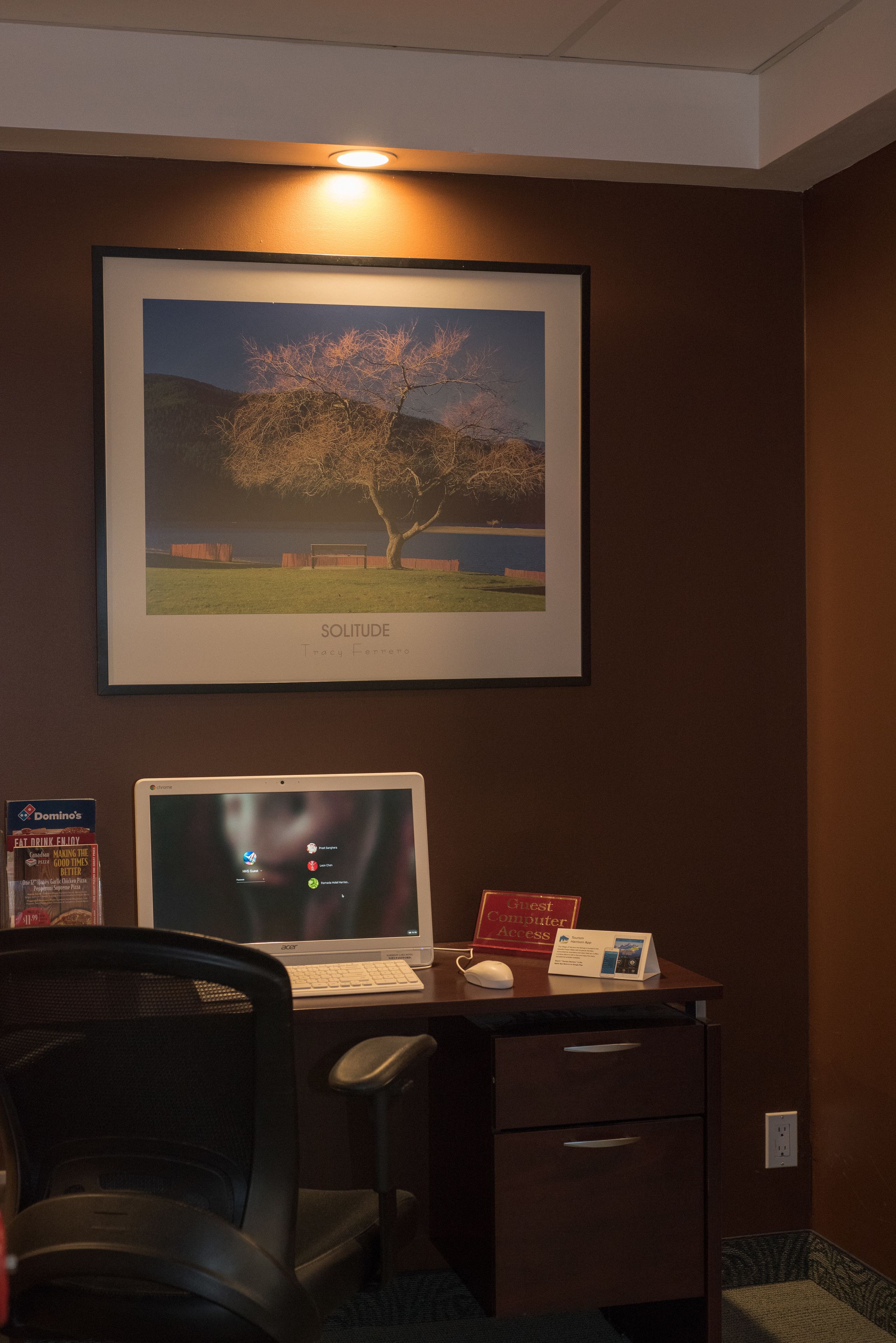 A desk with a computer, a framed picture of a tree, and a sign for computer access.