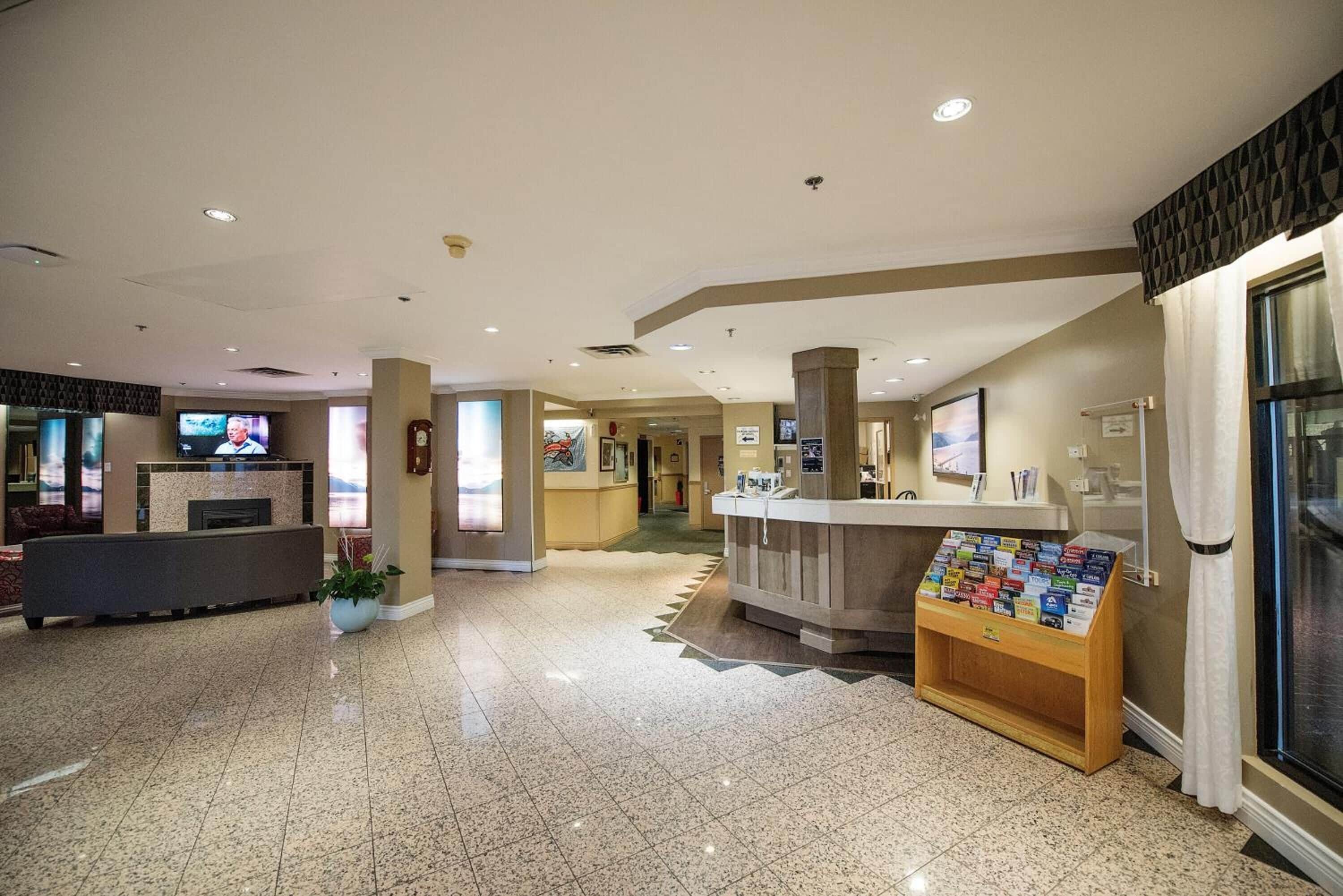 A hotel lobby with a reception desk, a fireplace, a clock, and a display of brochures.