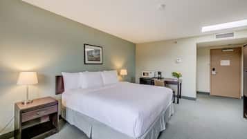 Habitación de hotel con una cama grande, mesitas de noche con lámparas, un escritorio con computadora, un microondas y una puerta con un letrero.