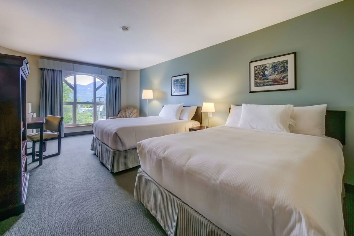 A hotel room with two beds, a desk, a chair, and a large window with a view.