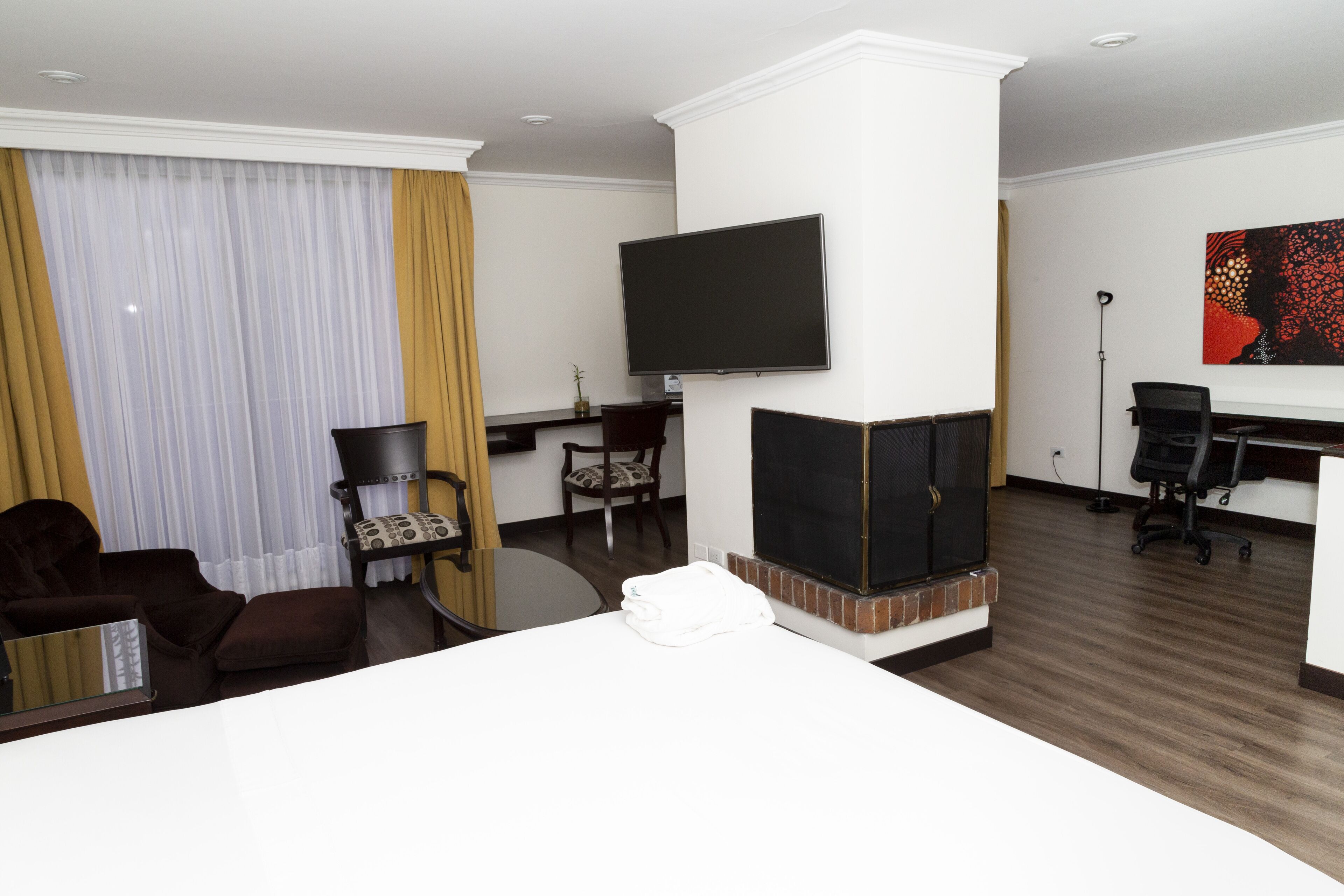 A hotel room with a flat-screen TV mounted on the wall, a fireplace, a desk, and a seating area with a sofa and chairs.
