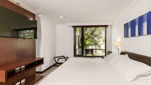 A hotel room with a large bed, a TV mounted on the wall, a balcony with a chair, and a view of greenery outside. - 101 Park House (Bogotá)