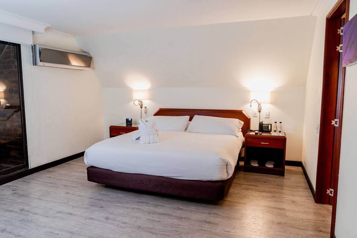 A neatly made bed with white linens, two bedside tables with lamps, and a wooden headboard.