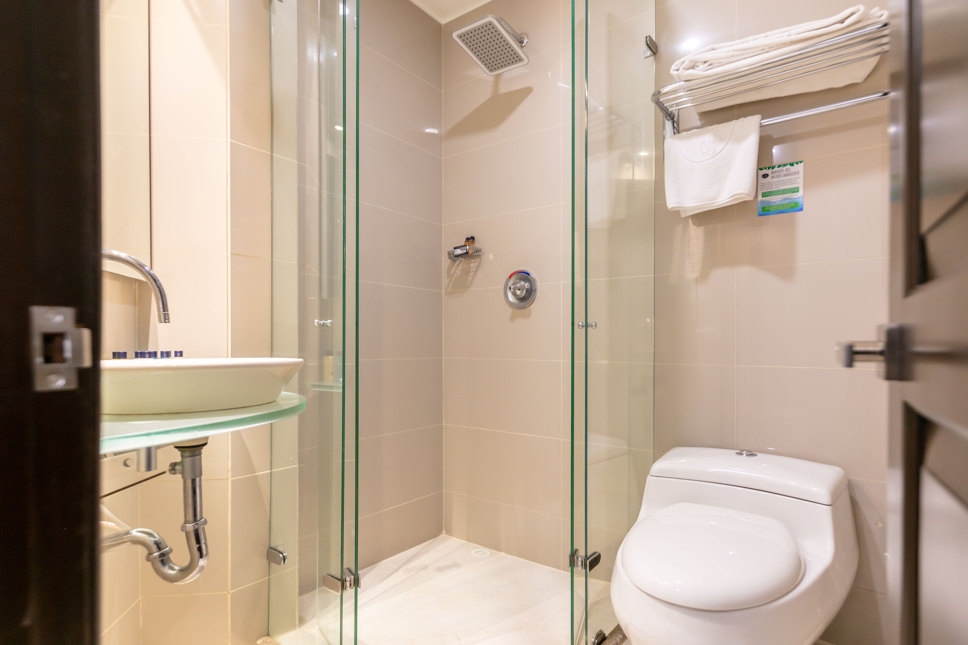 Un baño moderno con cabina de ducha de vidrio, inodoro blanco y lavamanos de vidrio.