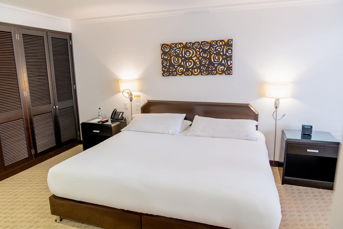 A neatly made bed with white linens, a wooden headboard, and two bedside tables with lamps.