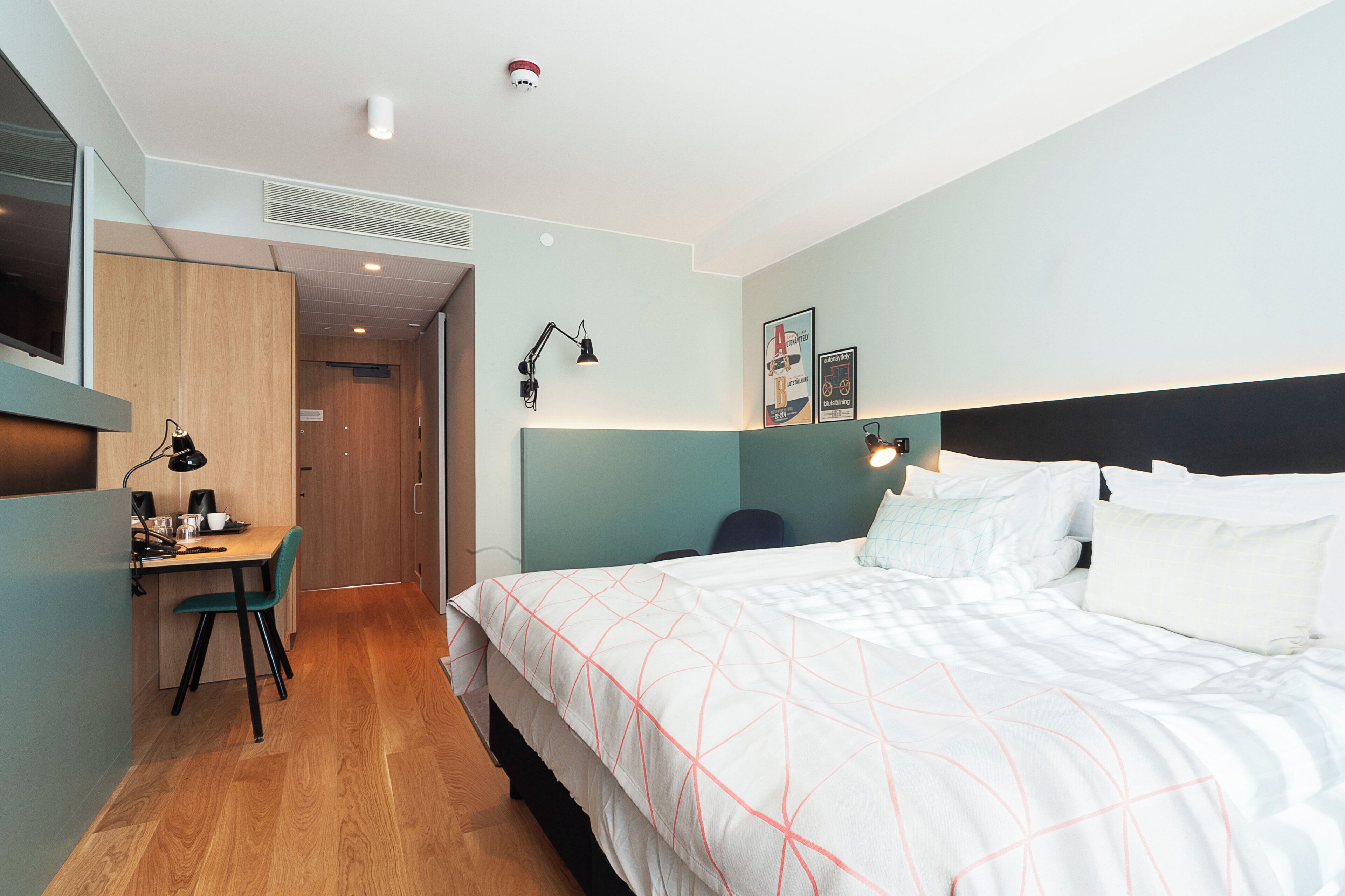 A hotel room with a bed, desk, chair, and a small kitchenette area.