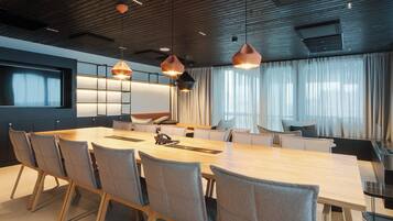 Una sala de conferencias moderna con una mesa larga, múltiples sillas e iluminación colgante.