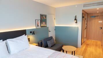A hotel room with a bed, a sofa, a small table, and a wall-mounted lamp.