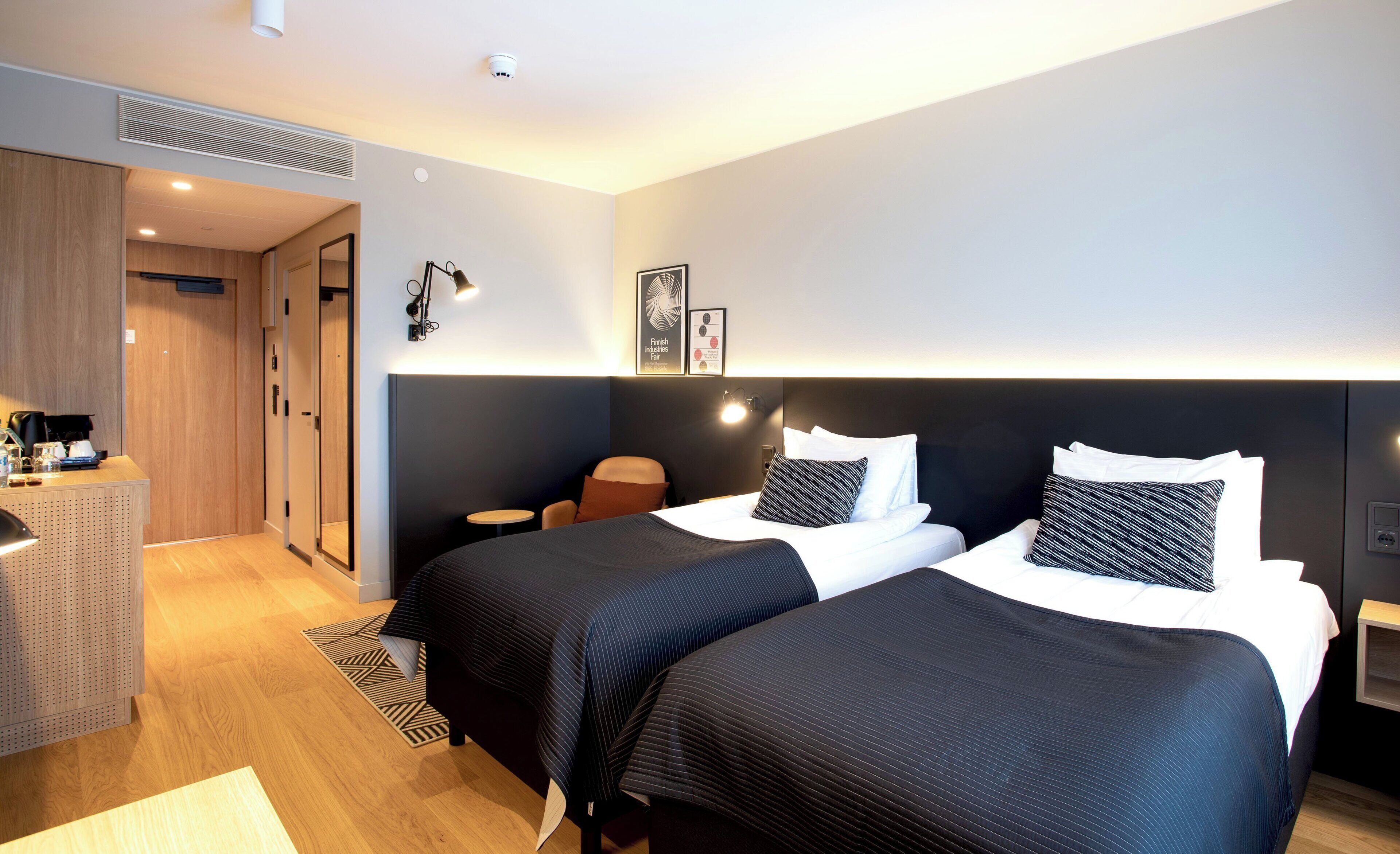 A hotel room with two beds, a desk, a chair, and a small table.
