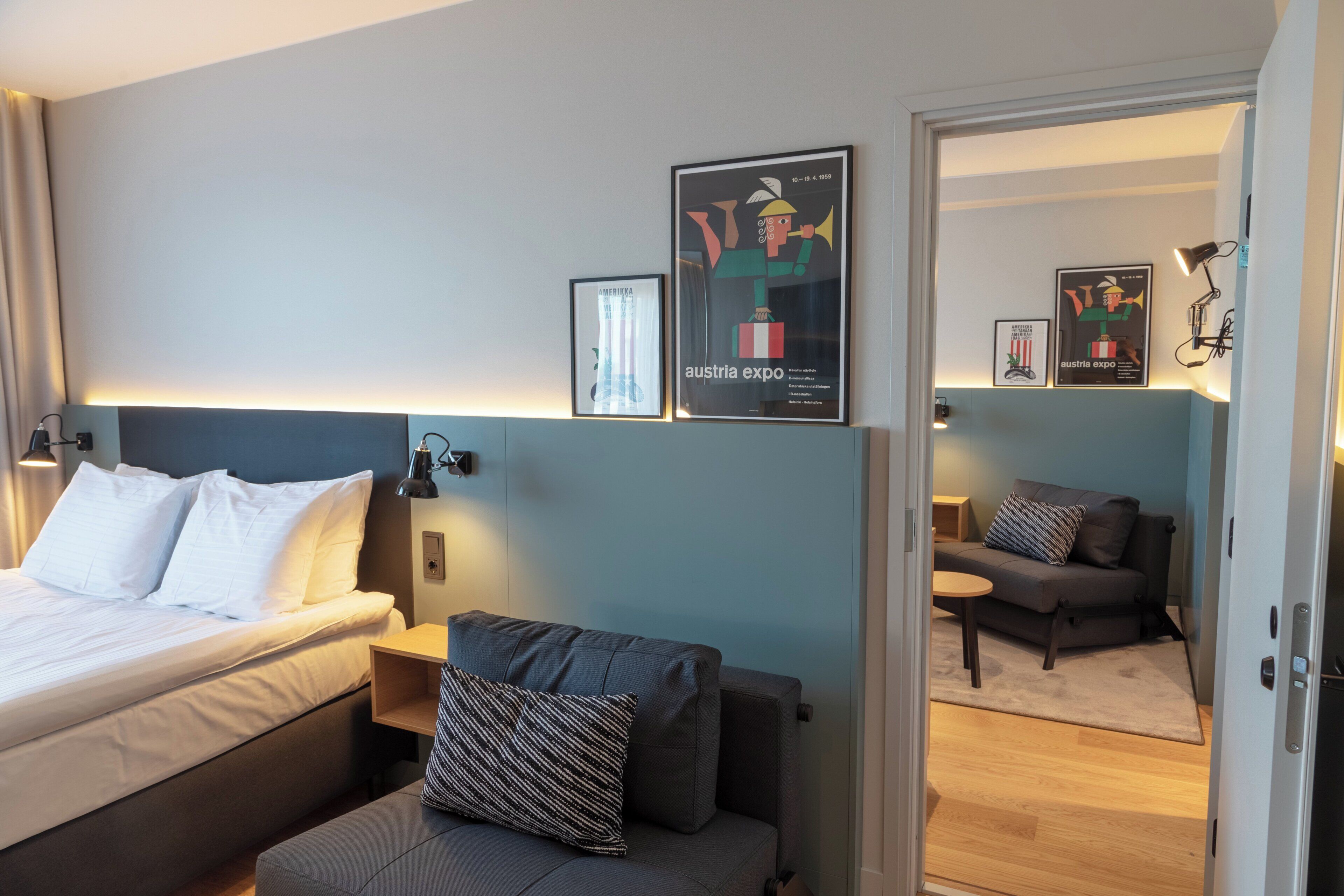 A hotel room with a bed, a sofa, a desk, and a chair. There are framed pictures on the wall.