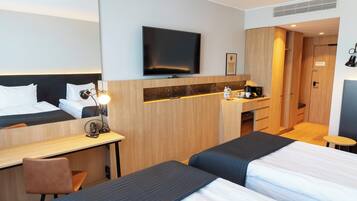 Habitación de hotel con dos camas, un escritorio, un espejo, una televisión y una pequeña kitchenette.