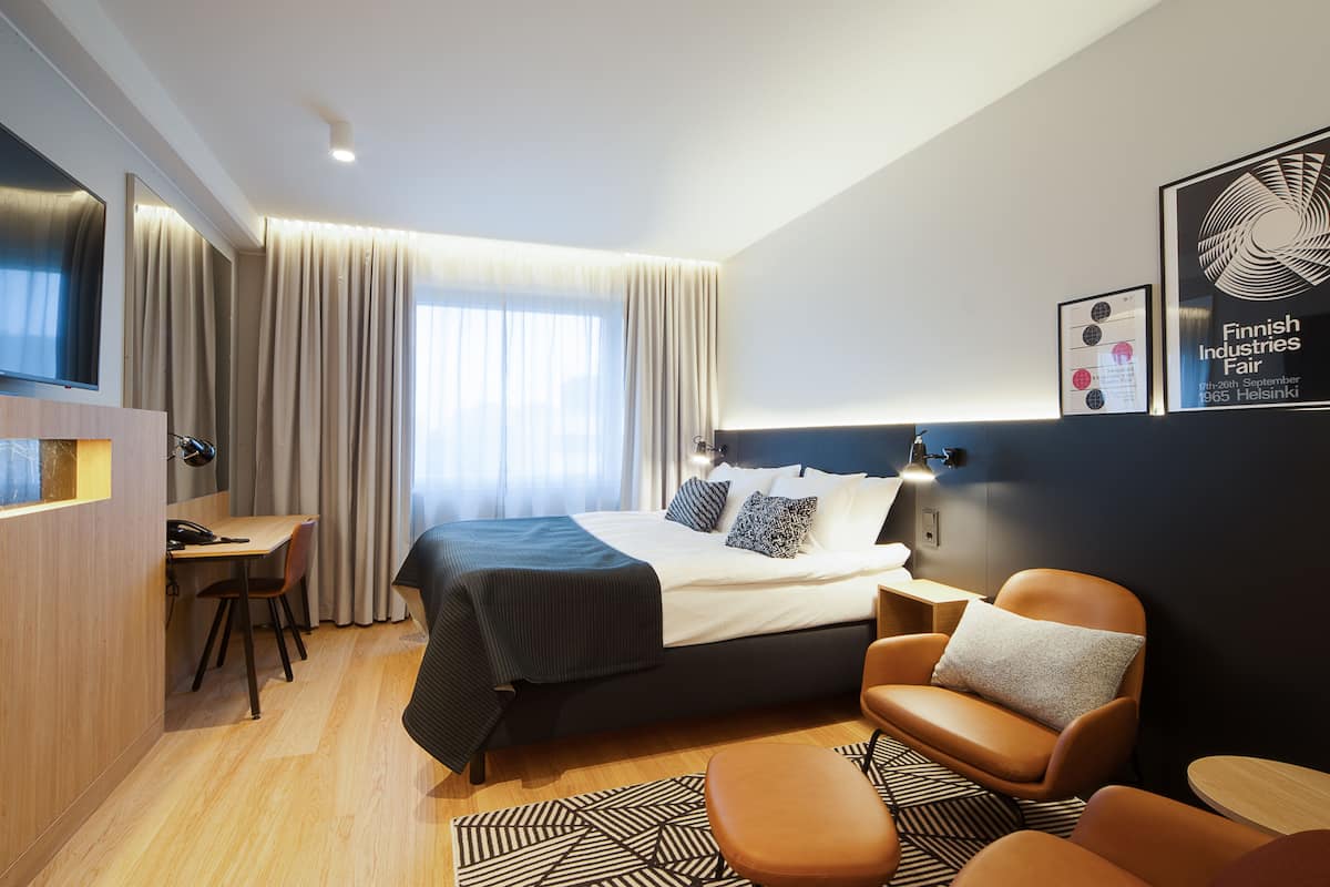 A modern hotel room with a large bed, a desk, and a seating area.