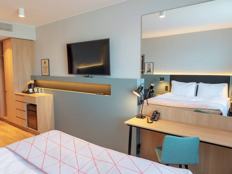 Una habitación de hotel con una cama, un escritorio, una silla, un televisor y un armario.