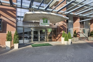 Holiday Inn -hotellin sisäänkäynti, jossa on lasinen katos, opastekyltti ja ruukkukasveja.