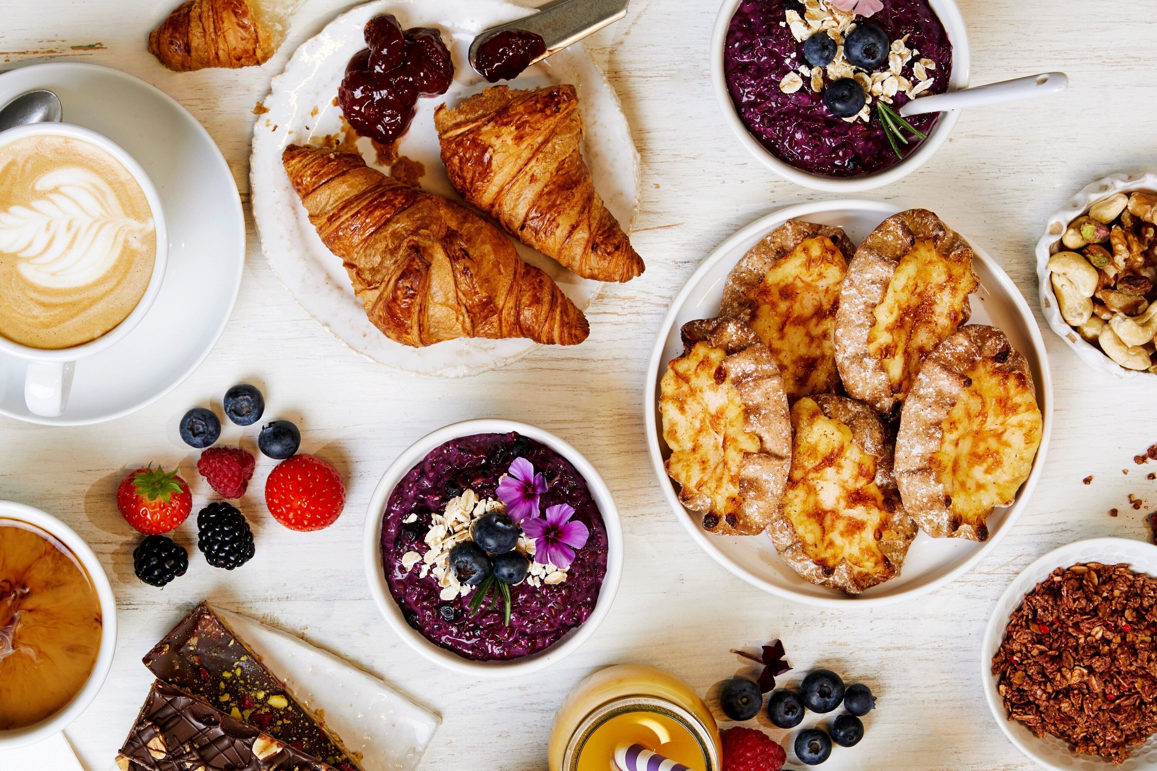 A variety of breakfast items including croissants, a bowl of oatmeal with blueberries, a cup of coffee, and a plate of waffles.