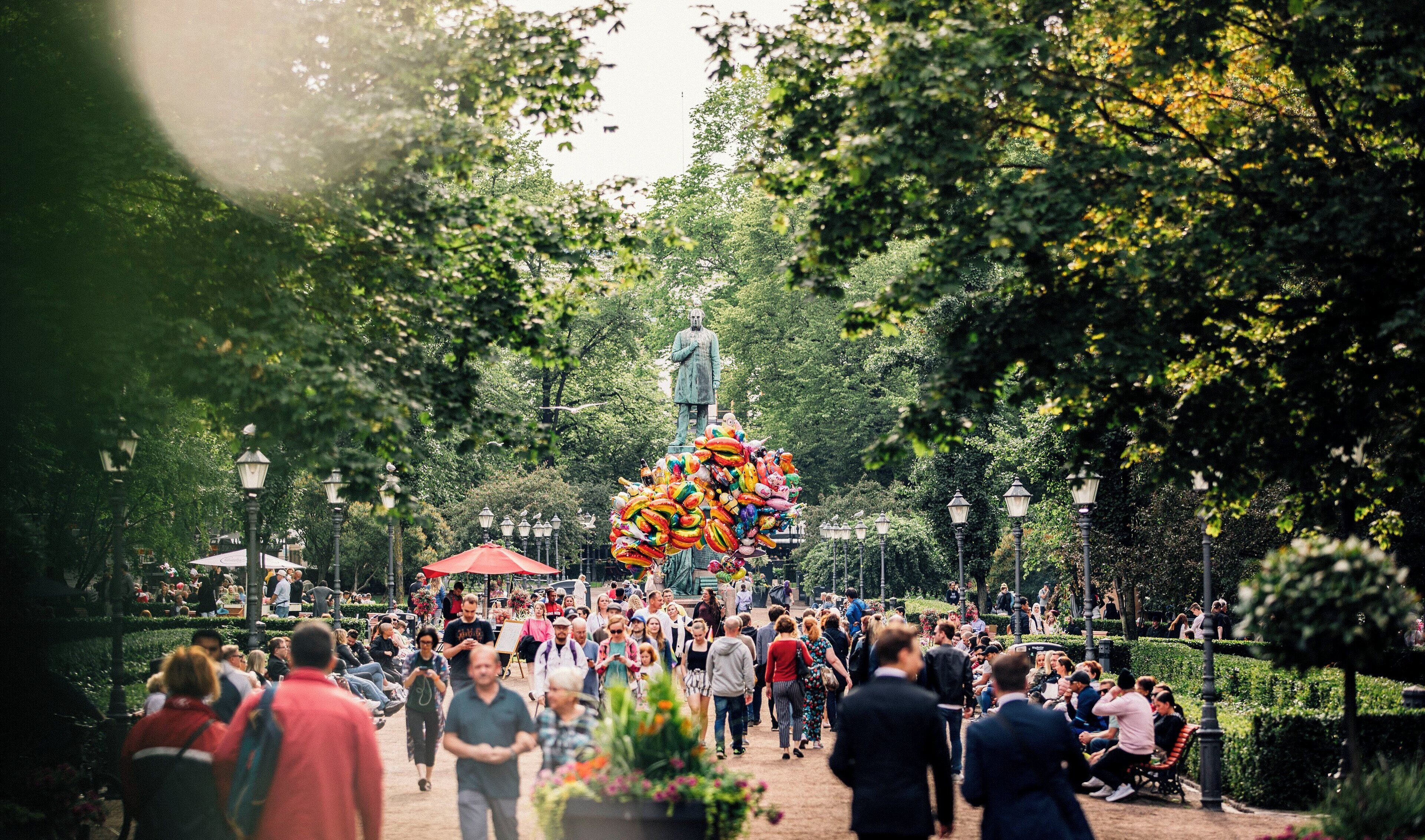 A public square with a statue, surrounded by trees and people.