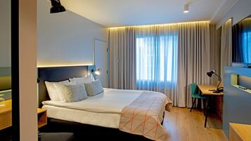 A modern hotel room with a large bed, a desk, a chair, and a TV.