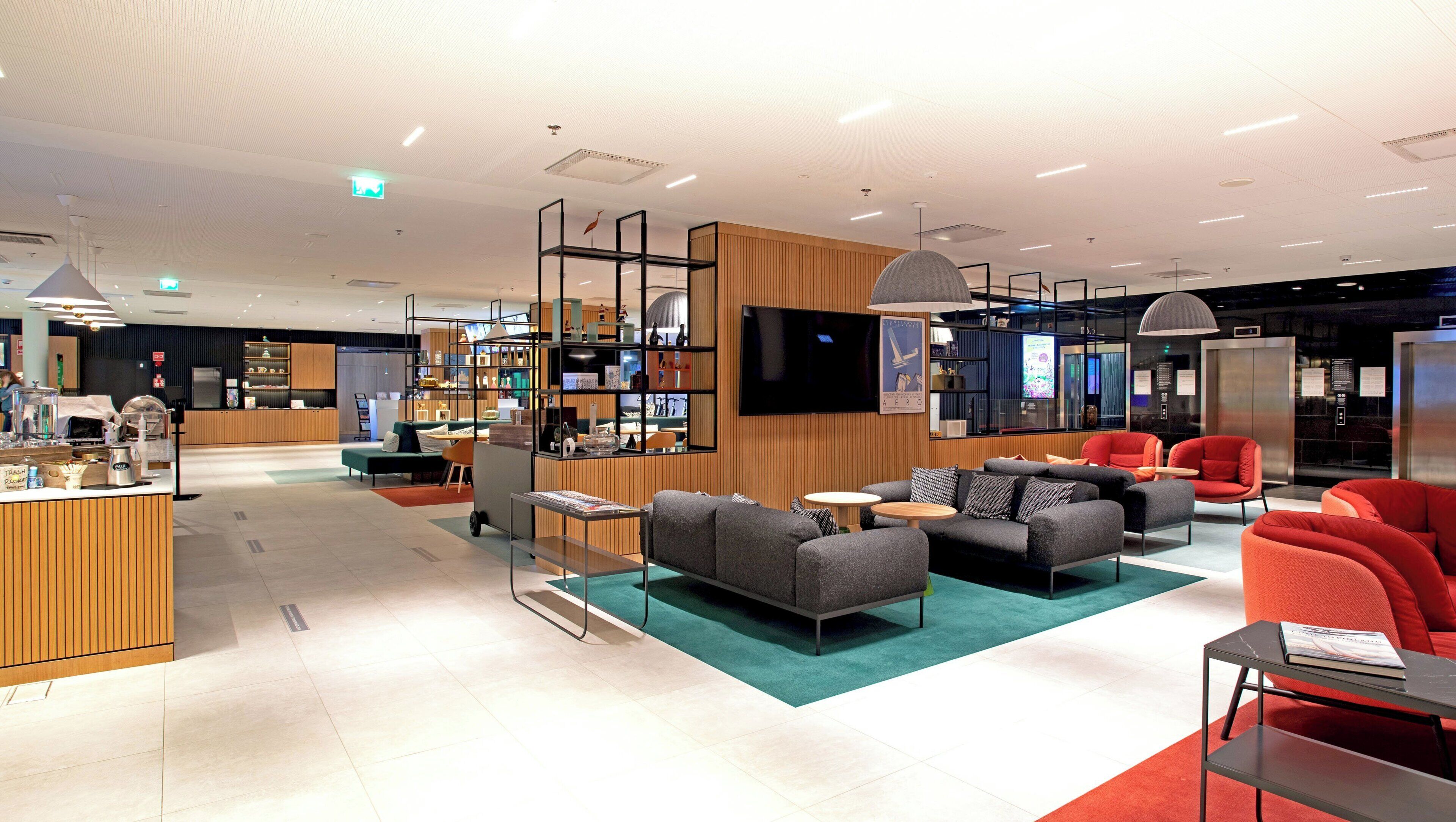 A modern lounge area with seating, a coffee station, and a TV screen.