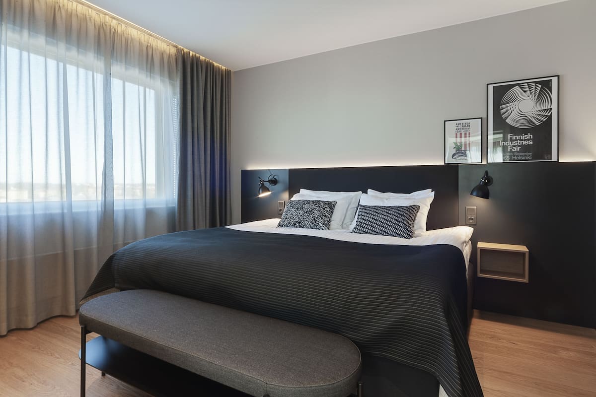 A modern hotel room with a large bed, bedside lamps, a bench, and artwork on the wall.