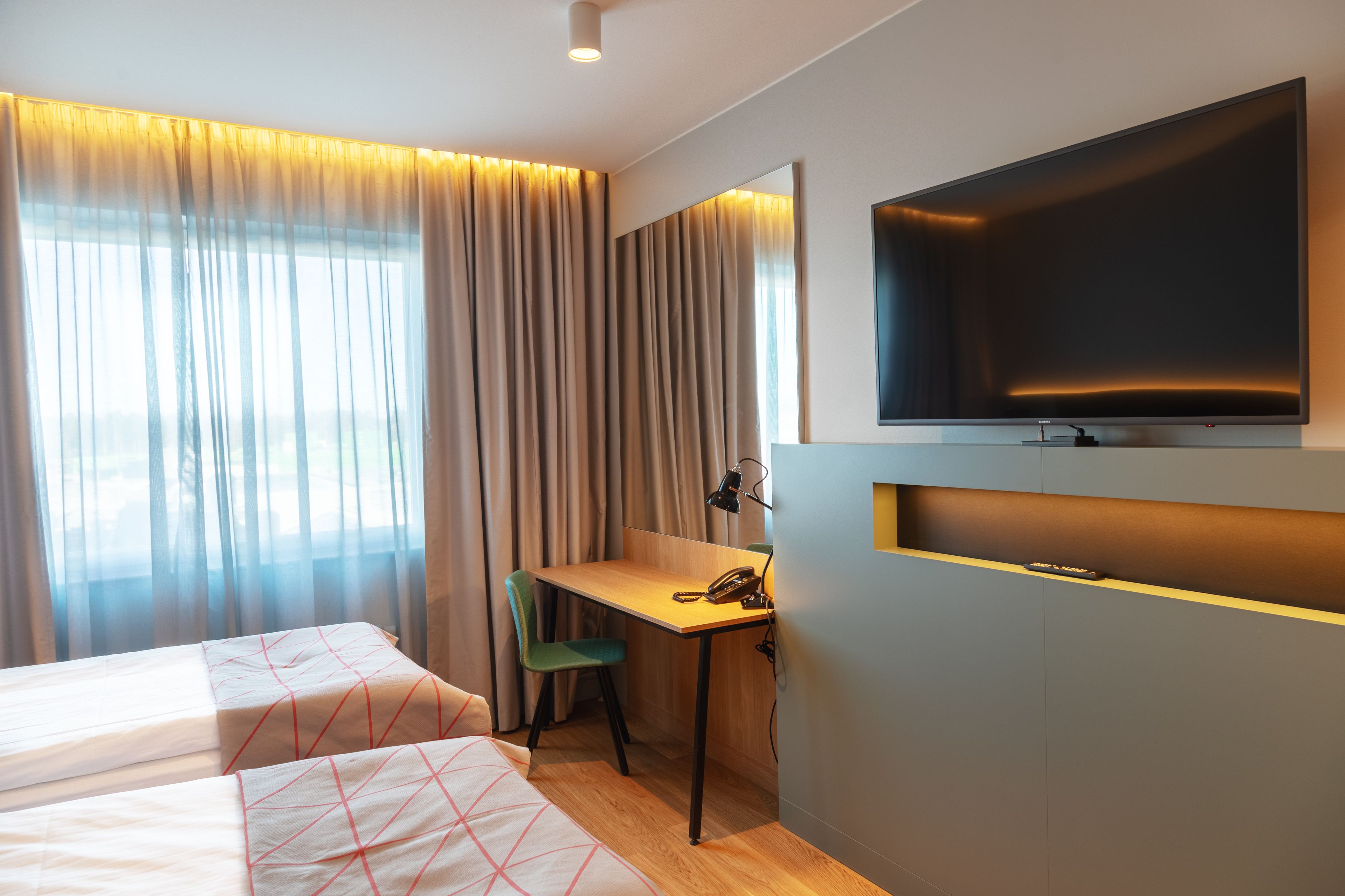 A hotel room with two beds, a desk, a chair, a TV, and a window with curtains.