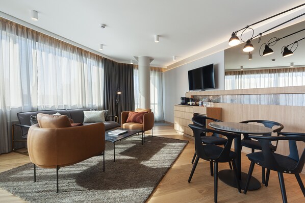 A modern living room with a sofa, armchair, coffee table, and dining area with chairs and a table. - Holiday Inn Helsinki - Expo by IHG (Helsinki)