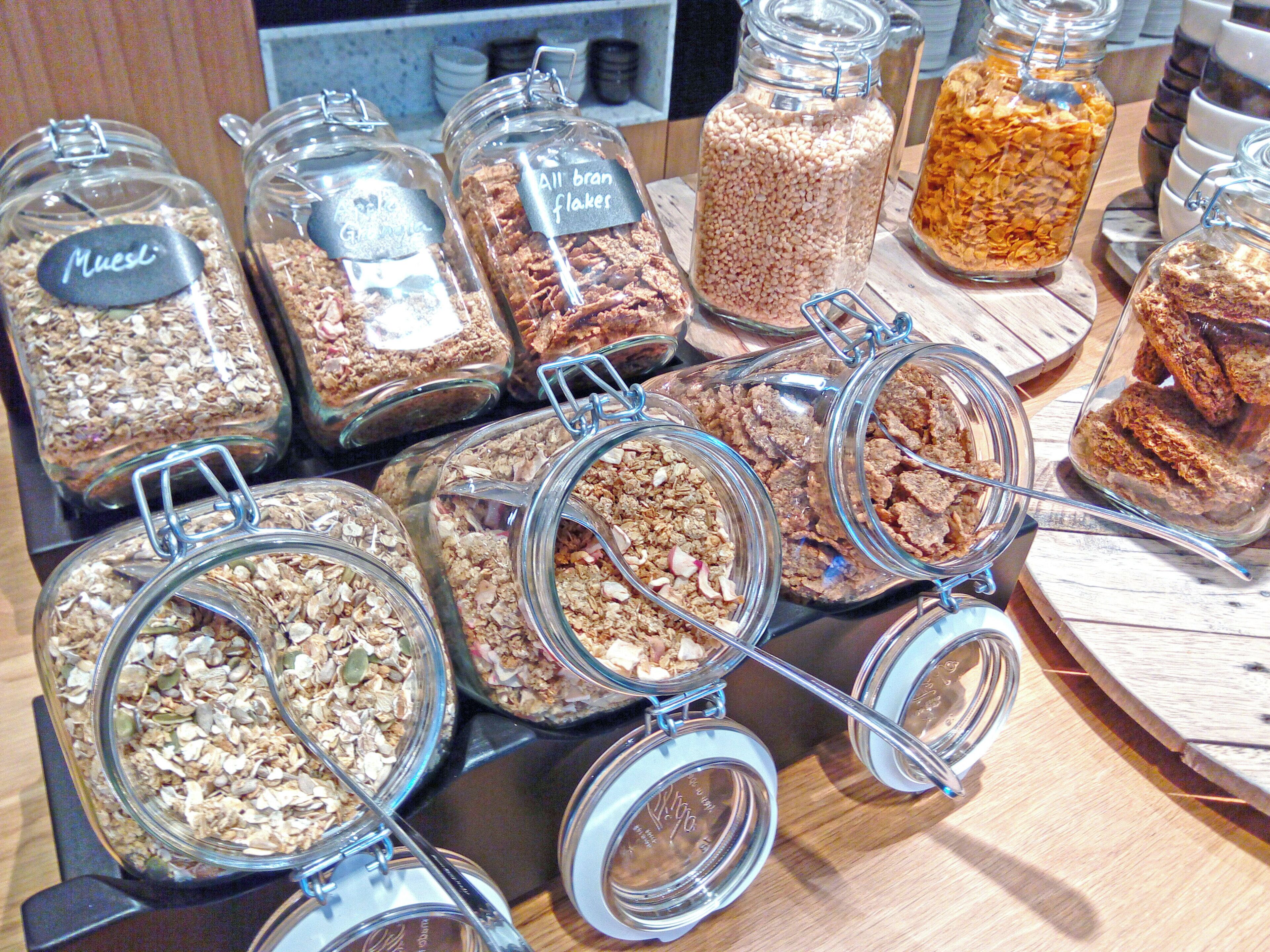 A variety of food items in glass jars with labels, arranged on a wooden surface.