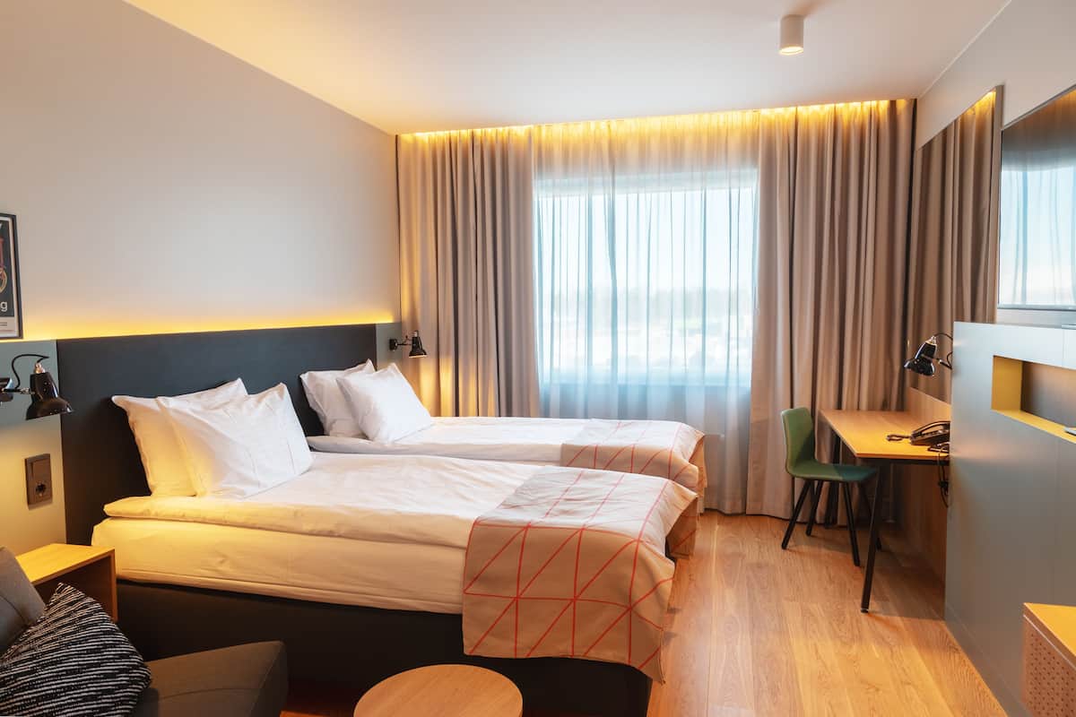 A hotel room with two beds, a desk, and a chair.