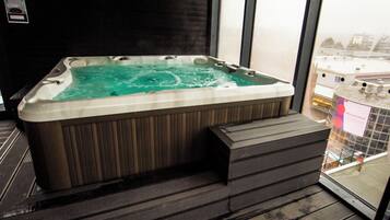 A hot tub with a wooden exterior and a view of a cityscape through a window.