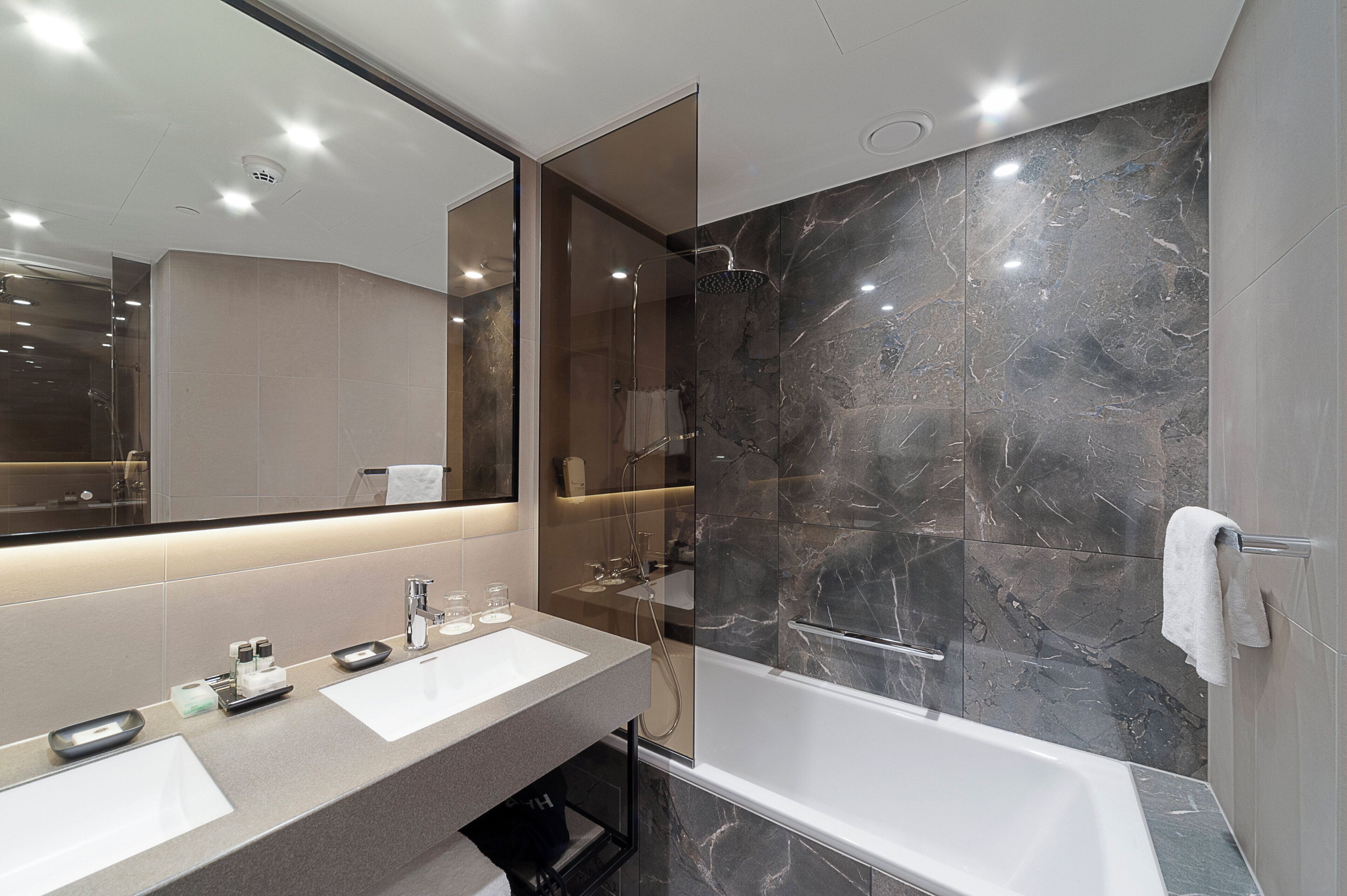 Une salle de bain moderne avec un meuble-lavabo à deux vasques, un grand miroir, une douche avec une porte en verre et des murs en marbre.