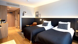 Moderni hotellihuone, jossa on kaksi sänkyä, työpöytä tuolilla ja pieni pöytä.