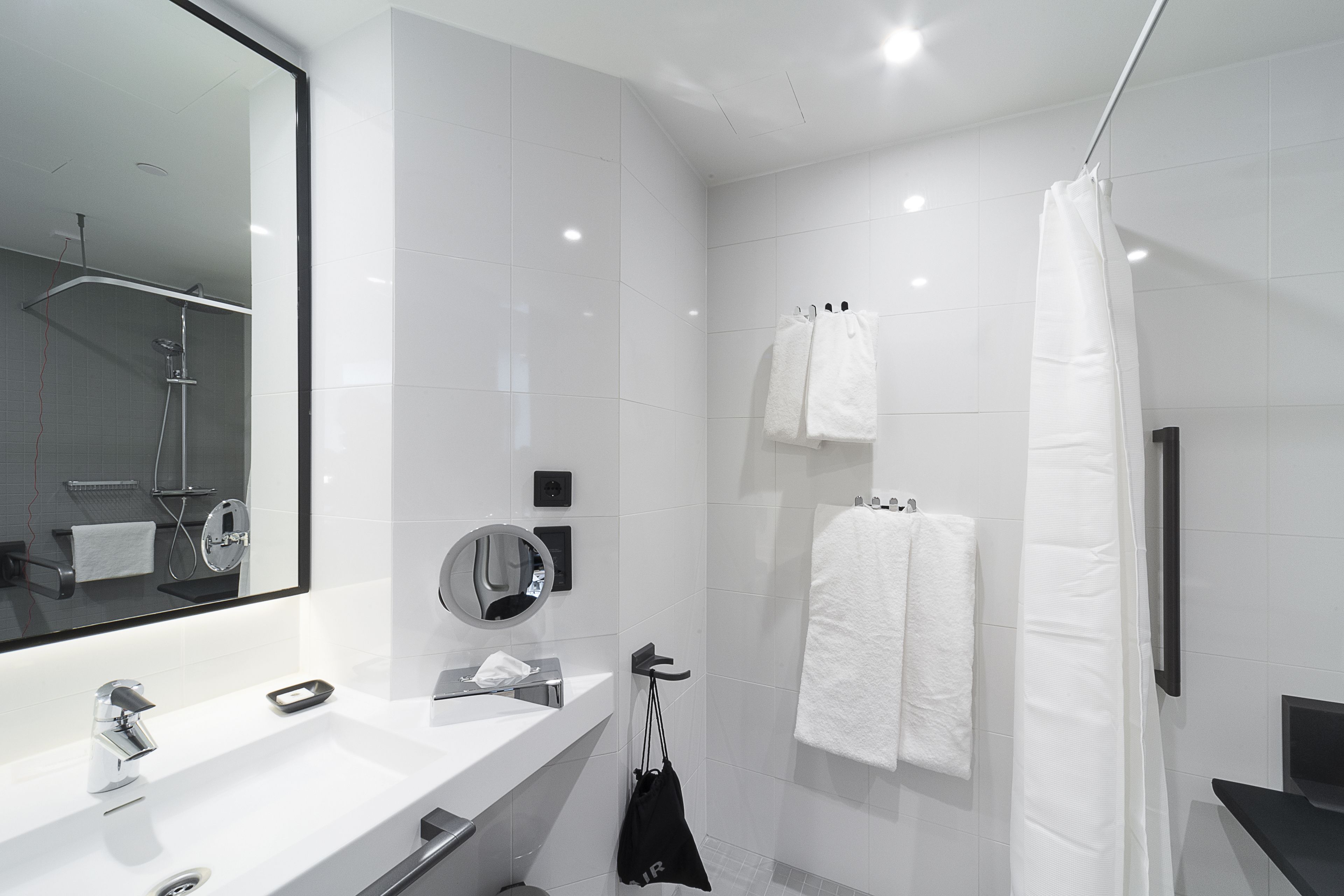 A modern bathroom with a large mirror, two sinks, a shower, and white towels.