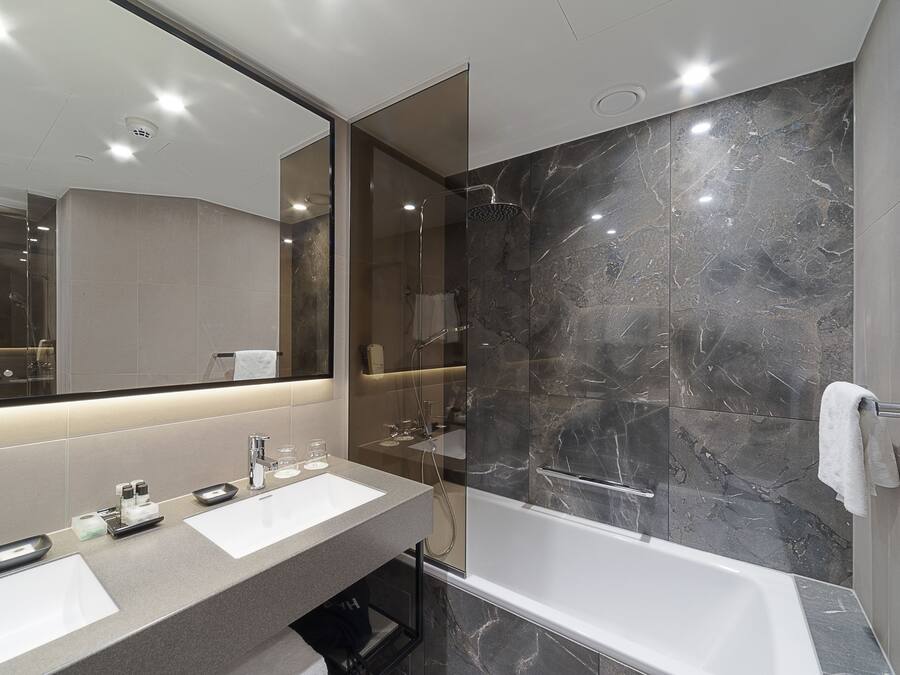 A modern bathroom with a large mirror, two sinks, a bathtub, and marble walls.
