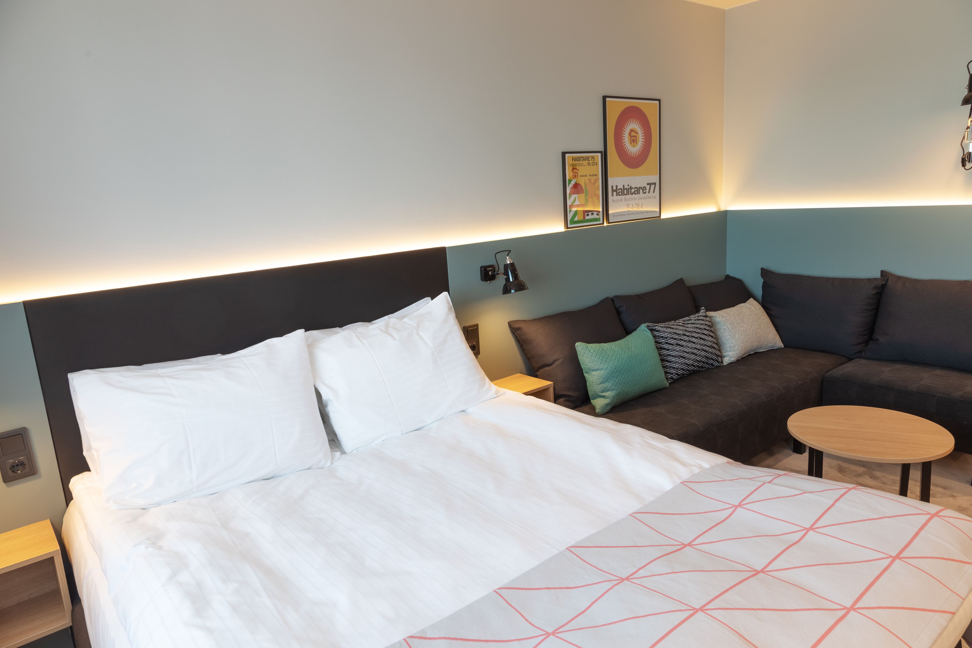 A hotel room with a large bed, a sofa, a small table, and a wall-mounted lamp.