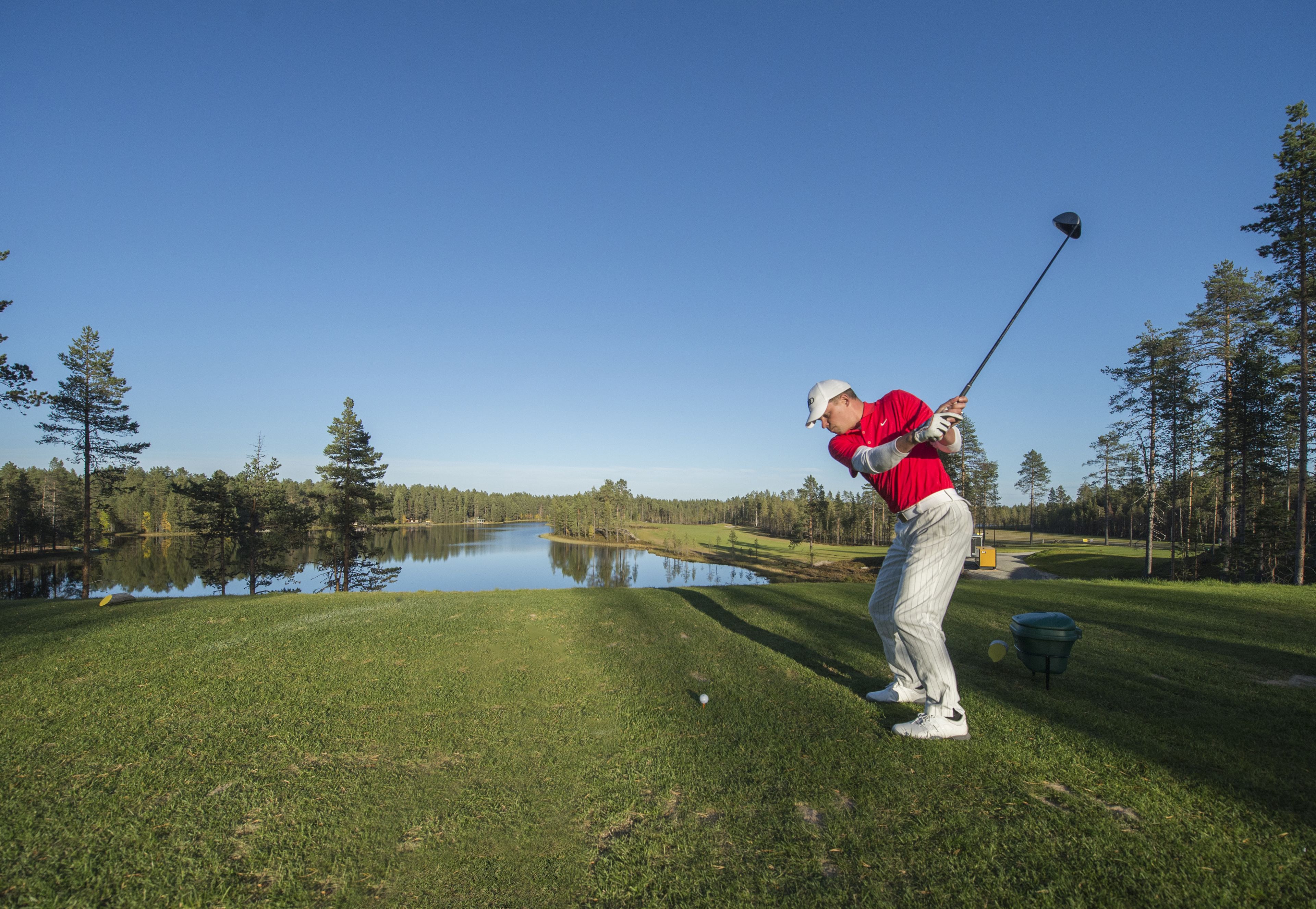 A golf course with a water body, trees, and a clear sky.