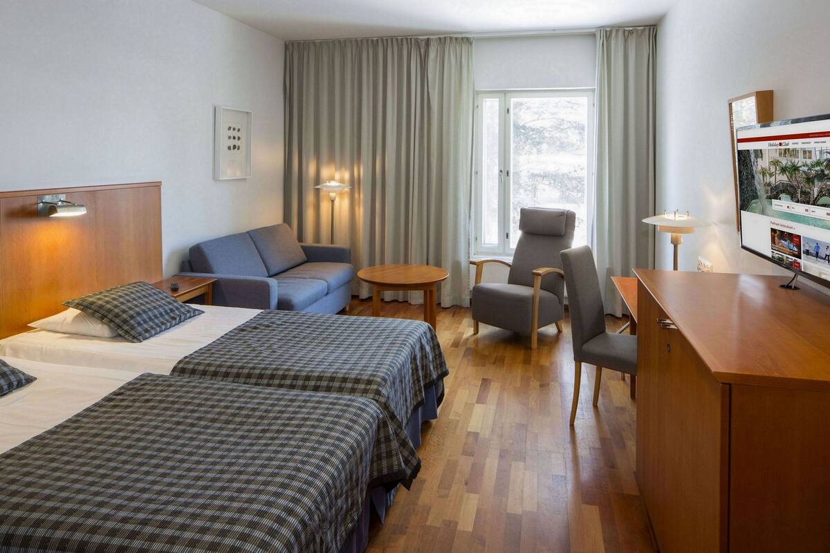A hotel room with two beds, a sofa, a desk, and a TV.
