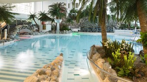 An indoor swimming pool with a tiled floor, surrounded by rocks and palm trees. - Holiday Club Kuusamon Tropiikki (Kuusamo)