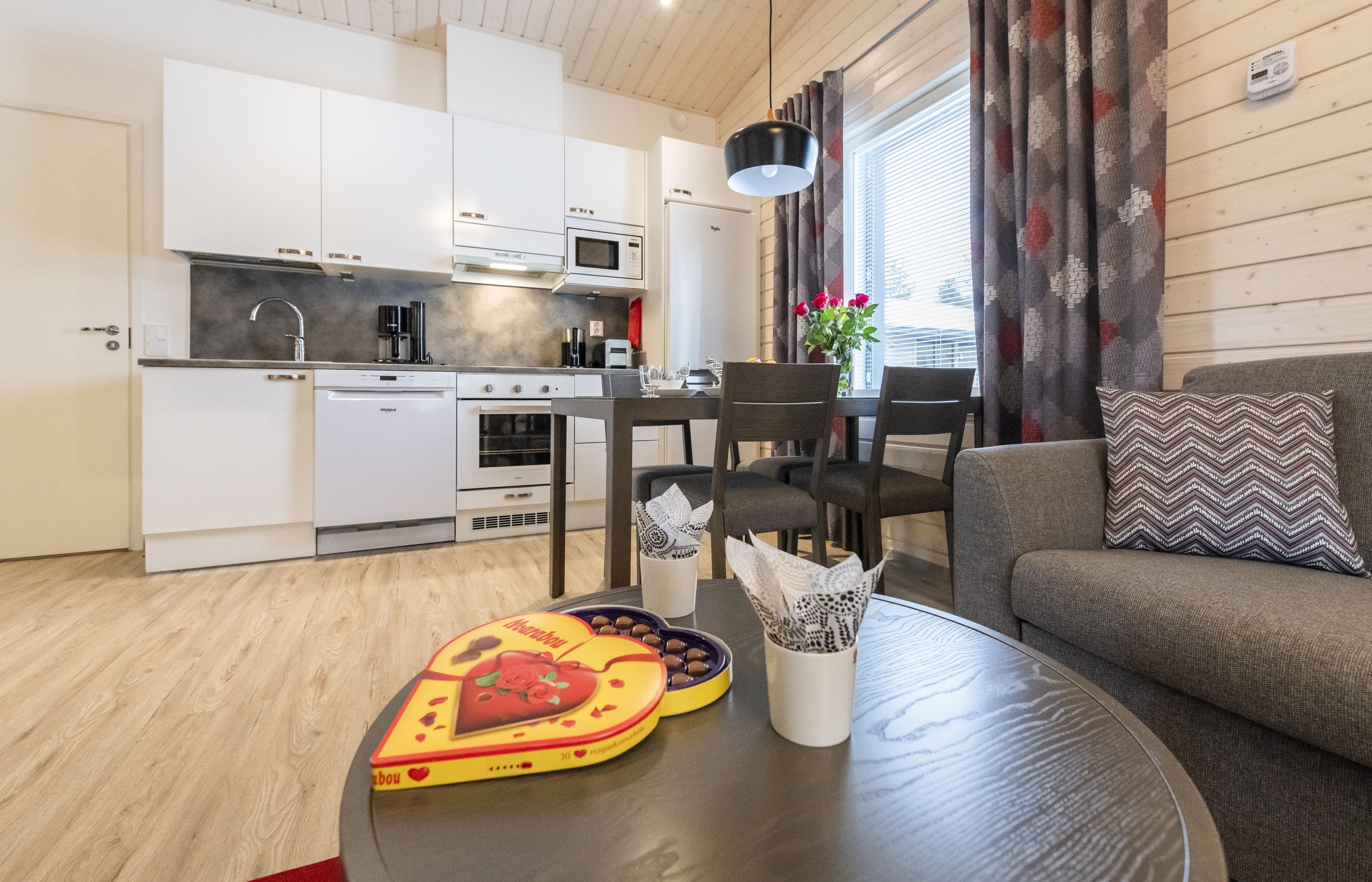Una cocina moderna con armarios blancos, microondas y lavavajillas. Hay un comedor con mesa, sillas y sofá.