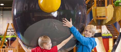 Two children interacting with a large, spherical play structure in an indoor play area.