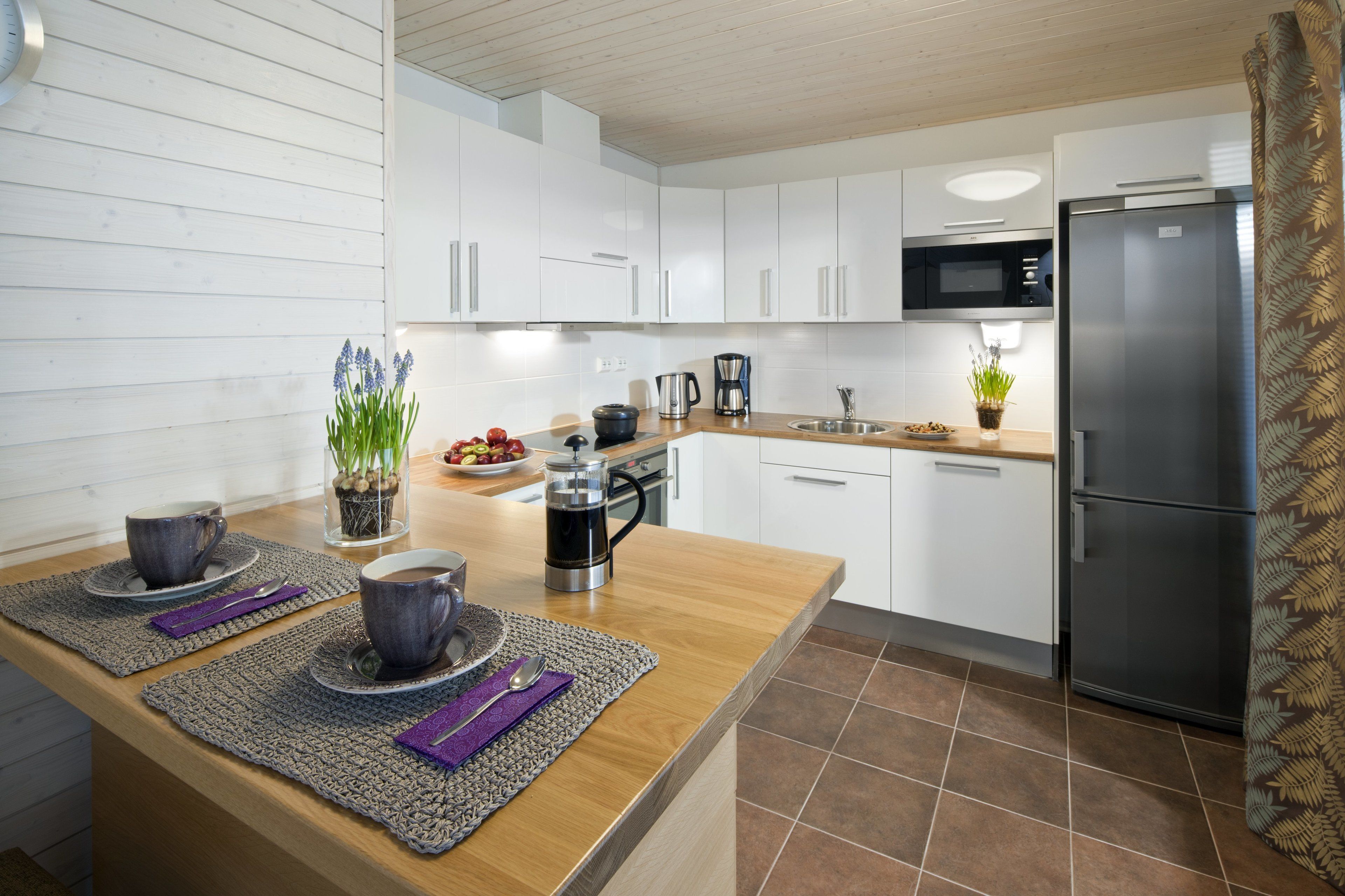 A modern kitchen with white cabinets, a stainless steel refrigerator, and a wooden countertop.