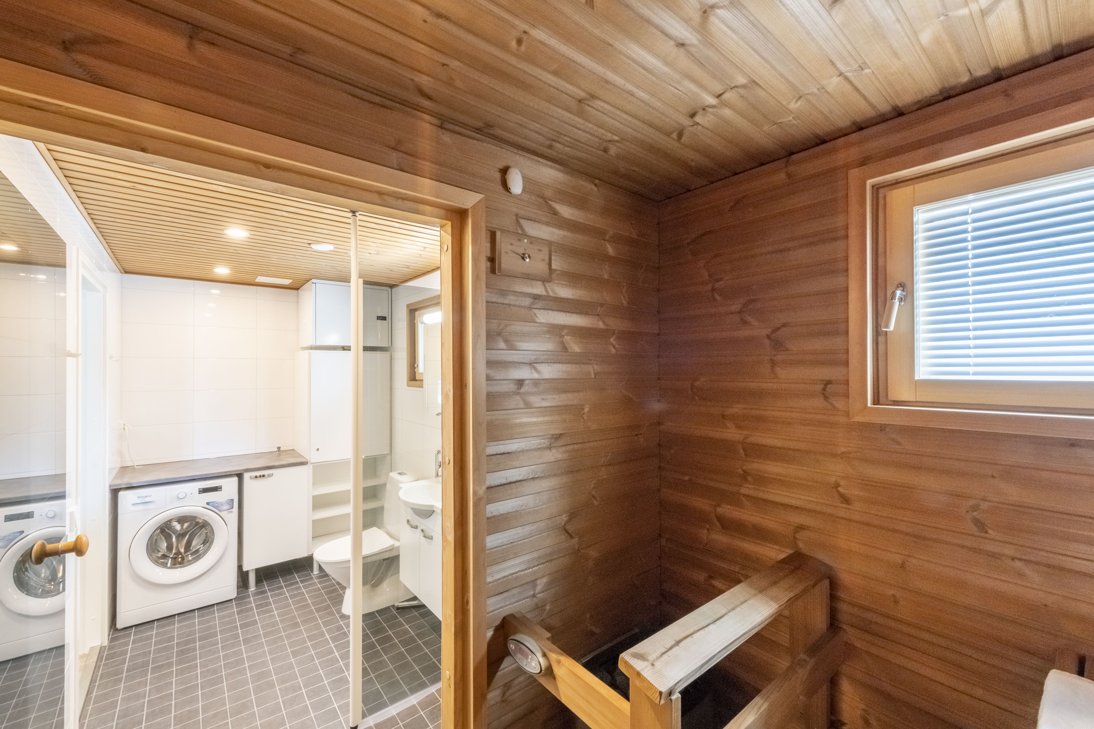 A compact bathroom with a wooden interior, a washing machine, a toilet, and a window.
